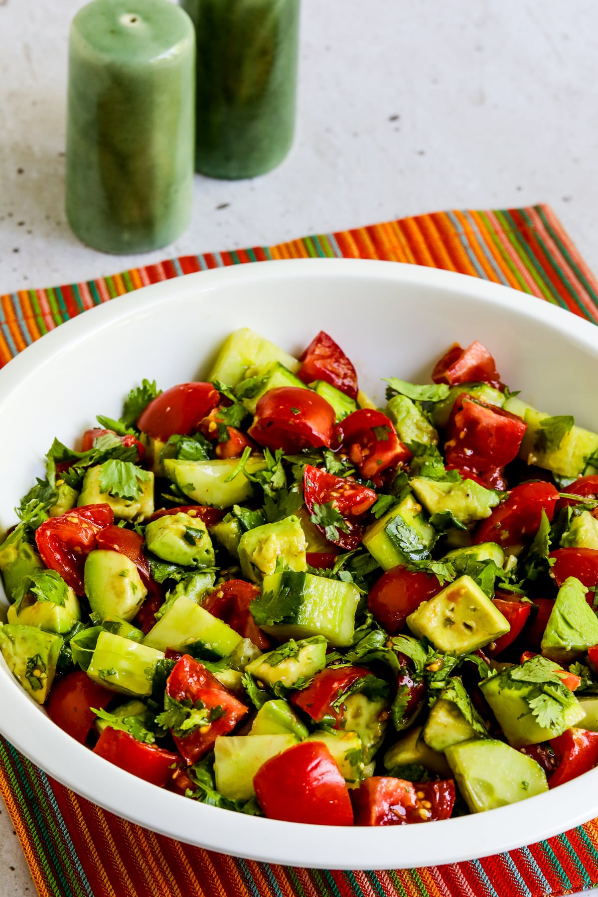 Tomato Salad with Cucumbers, Avocado, and Cilantro shown in serving bowl with striped napkin.