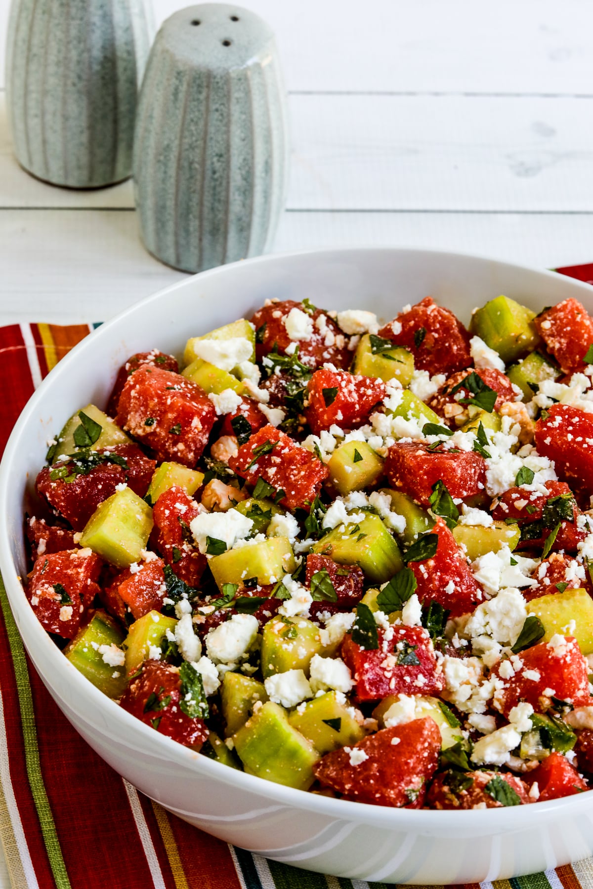 Watermelon and Cucumber Salad in white serving bowl with salt-pepper in back.