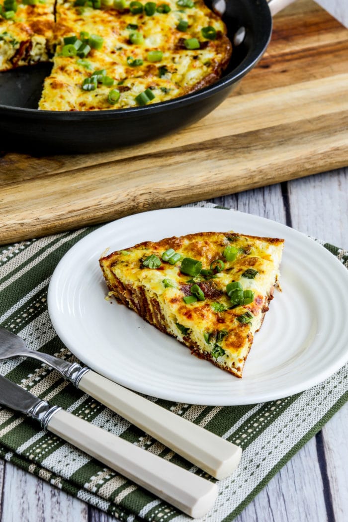 Close-up shot of Bacon Frittata with Two Cheeses one slice on serving dish and frittata in pan in background