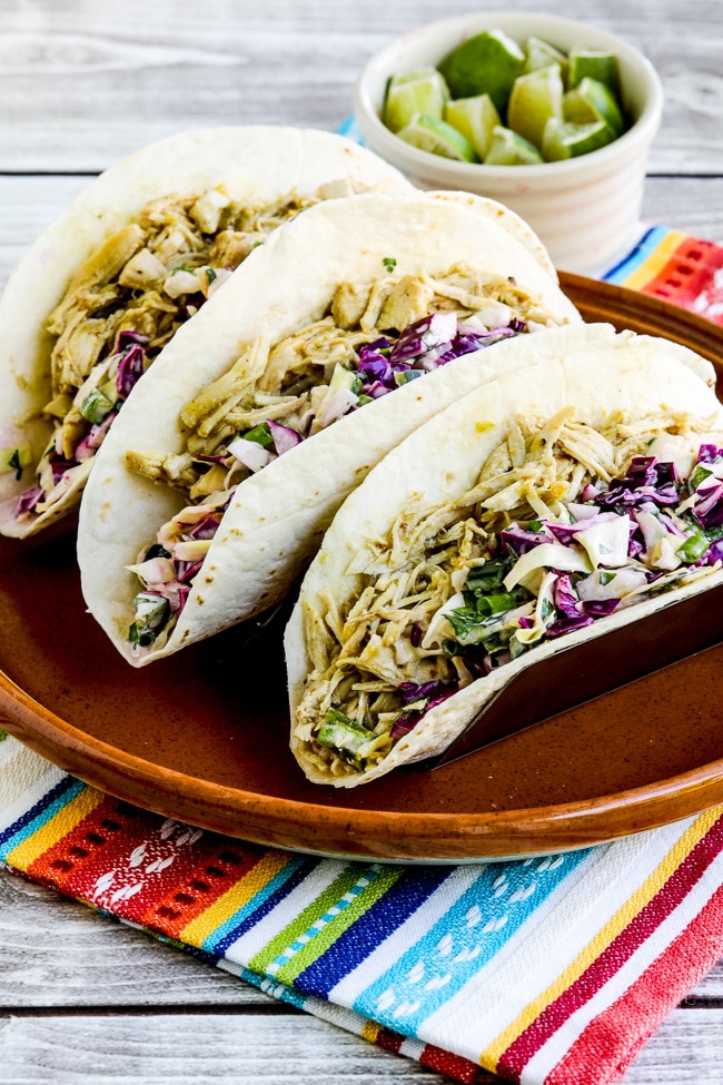 Green Chile Chicken Tacos shown on serving plate with cut limes on the side.
