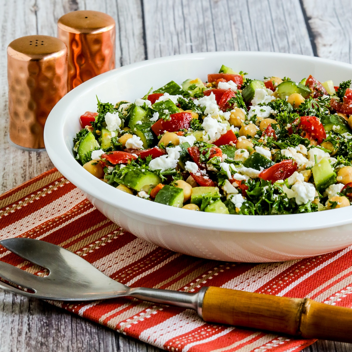 Square image for Tomato Cucumber Chickpea Salad showing salad in large bowl on napkin with serving fork.