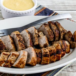 Pan-fried pork tenderloin with creamy mustard sauce shown on serving platter with fork and sauce in back.