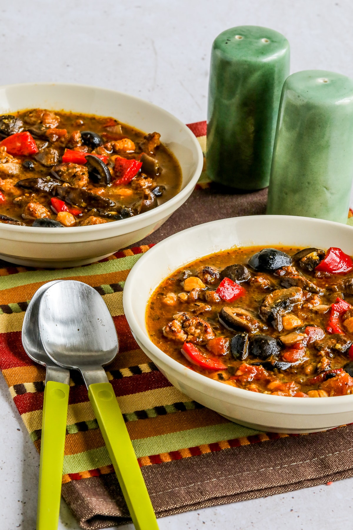 Updated photo for Sausage and Chickpea stew showing bowl bowls of stew with spoons and salt-pepper shakers.