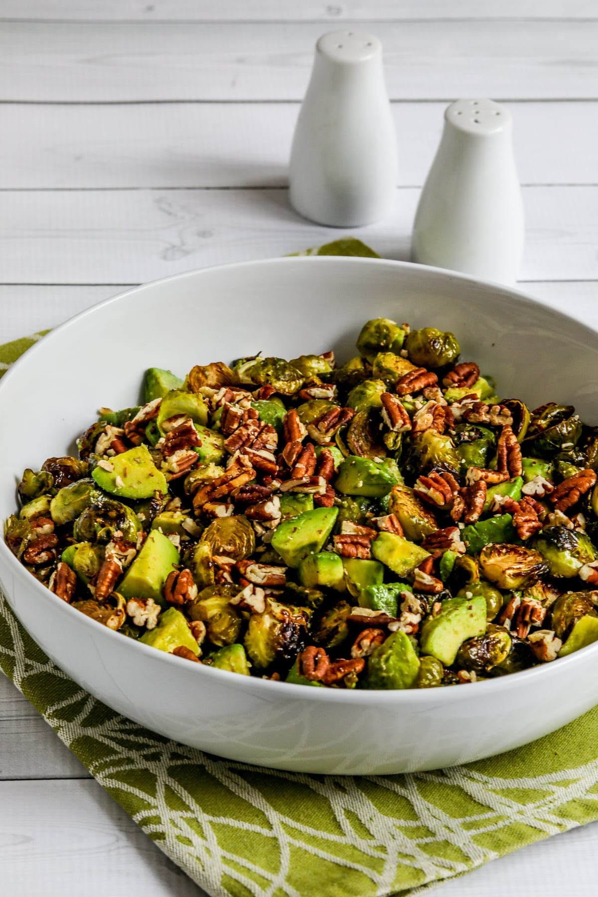 Roasted Brussels Sprouts with Avocados and Pecans in serving bowl with salt-pepper in background