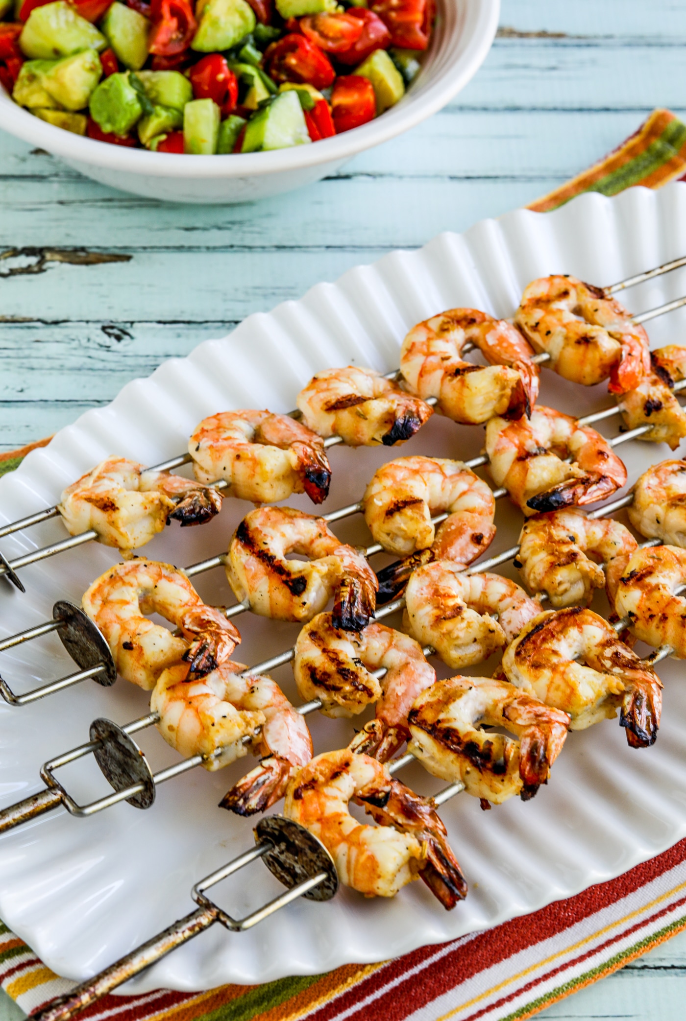 Grilled Shrimp Skewers on serving plate with bowl of tomato-avocado salsa.